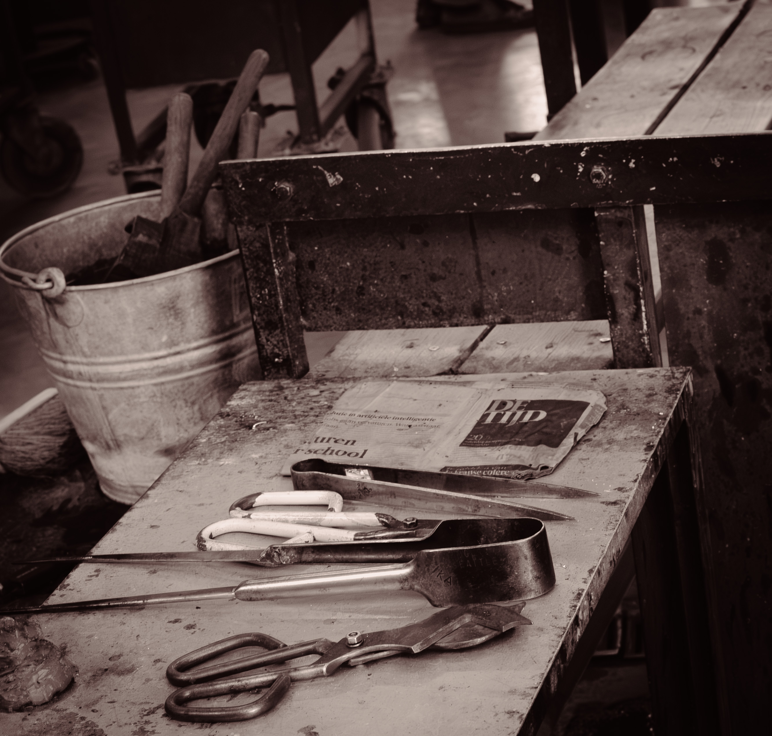 Detail van een werktafel in het glasatelier met scharen, tangen, gereedschap en een krant.